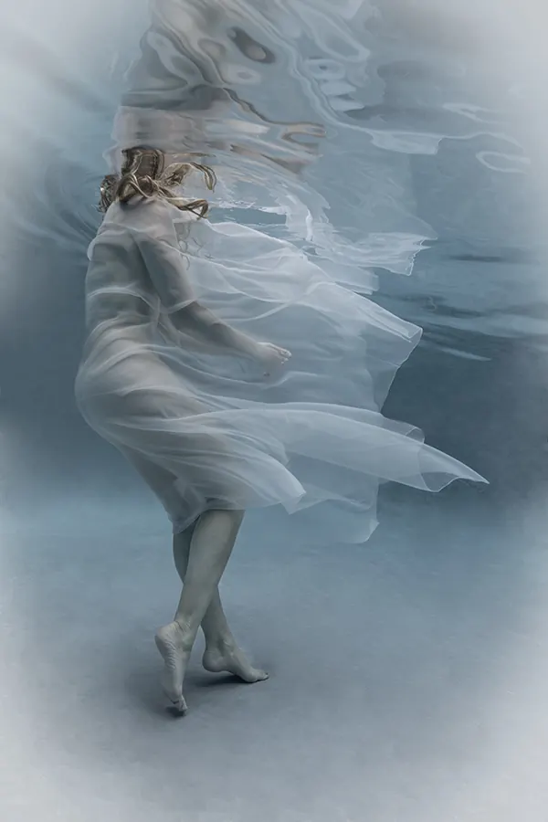 The Current — a figure in flowing white fabric suspended underwater in pale blue light