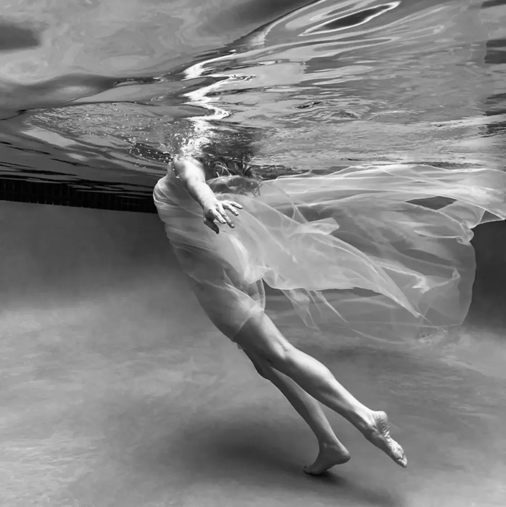Pool Dance — a black and white underwater photograph of a dancer in flowing sheer fabric