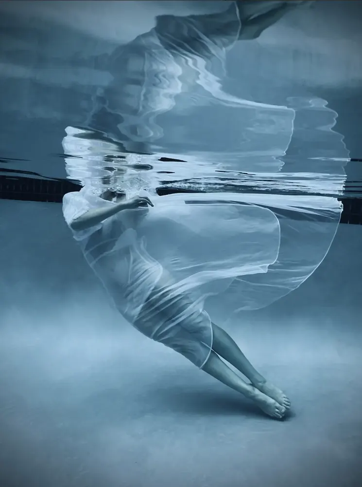 Underwater Linnea — a figure in a translucent white gown drifting beneath the surface of a pool
